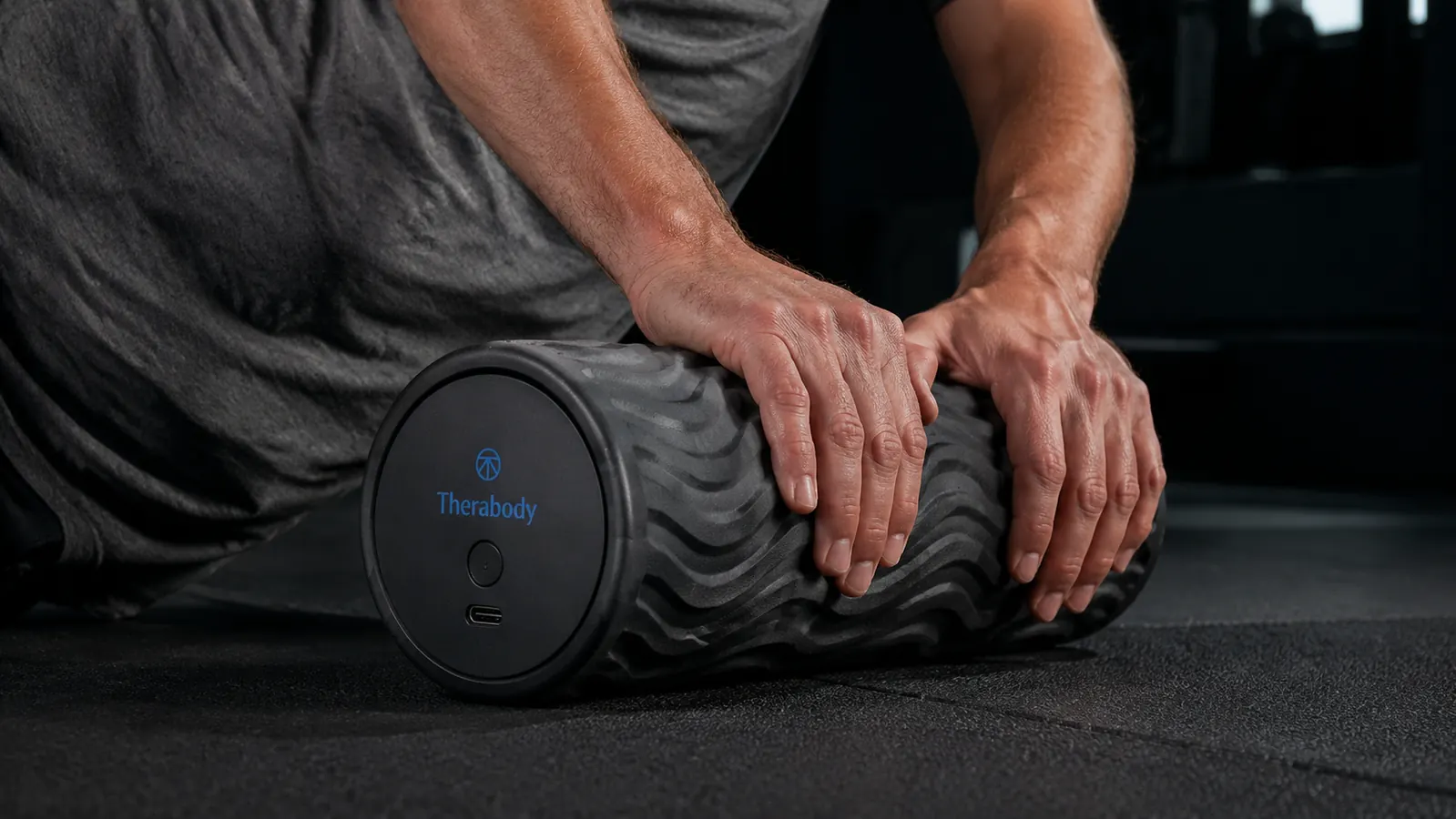 Therabody WaveRoller standing upright on a gym mat showing its wave-textured surface and USB-C charging port on the end cap