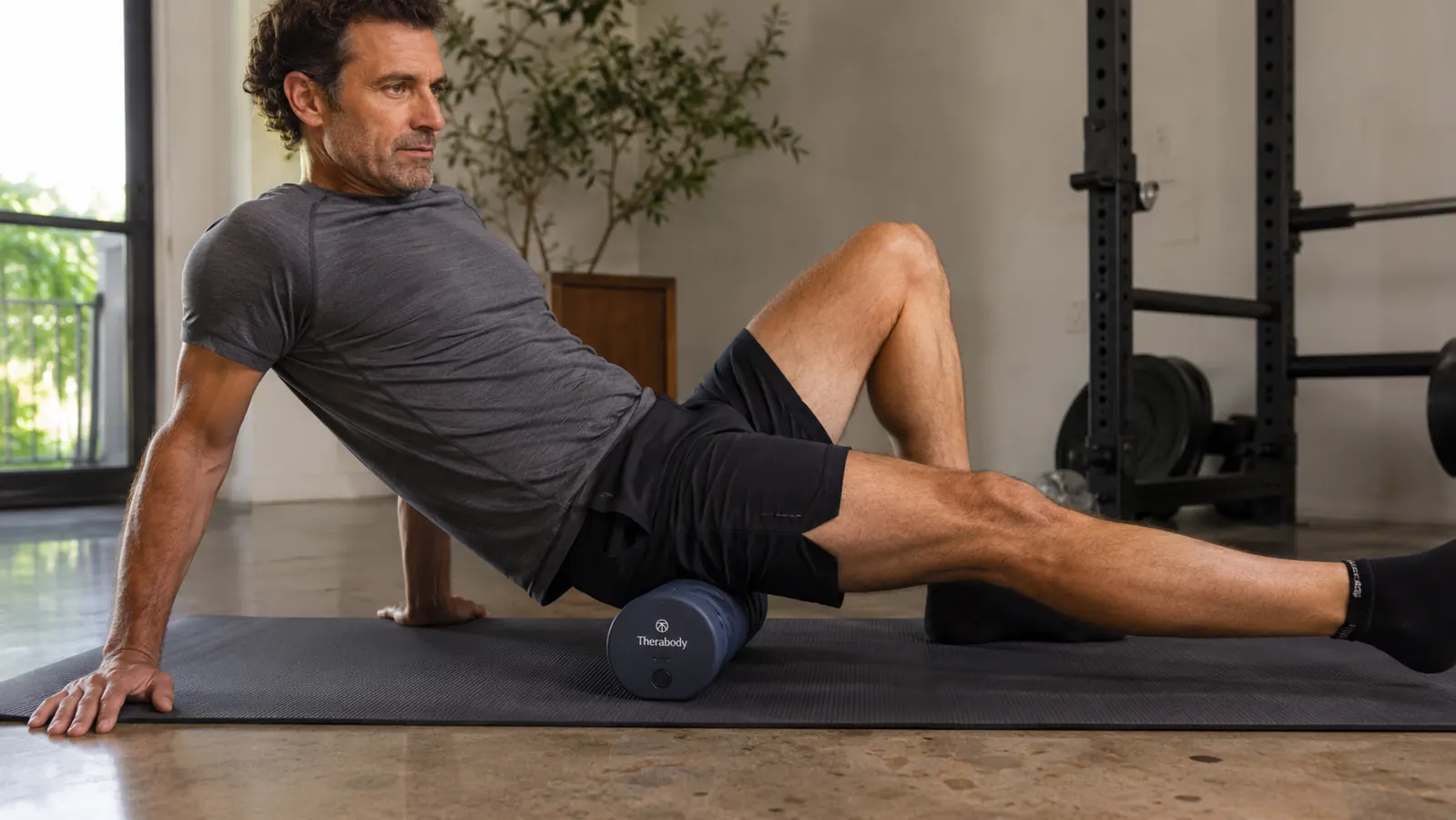 Person using the WaveRoller on their hip flexor area while lying on a yoga mat with one knee bent, focused expression